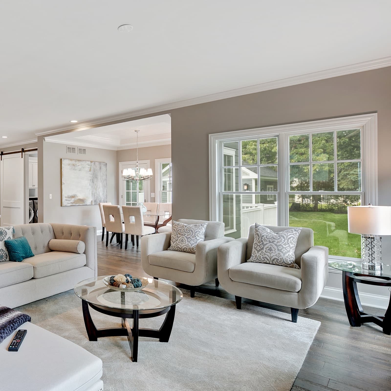 A bright living room with armchairs by a large window and a lamp switched on