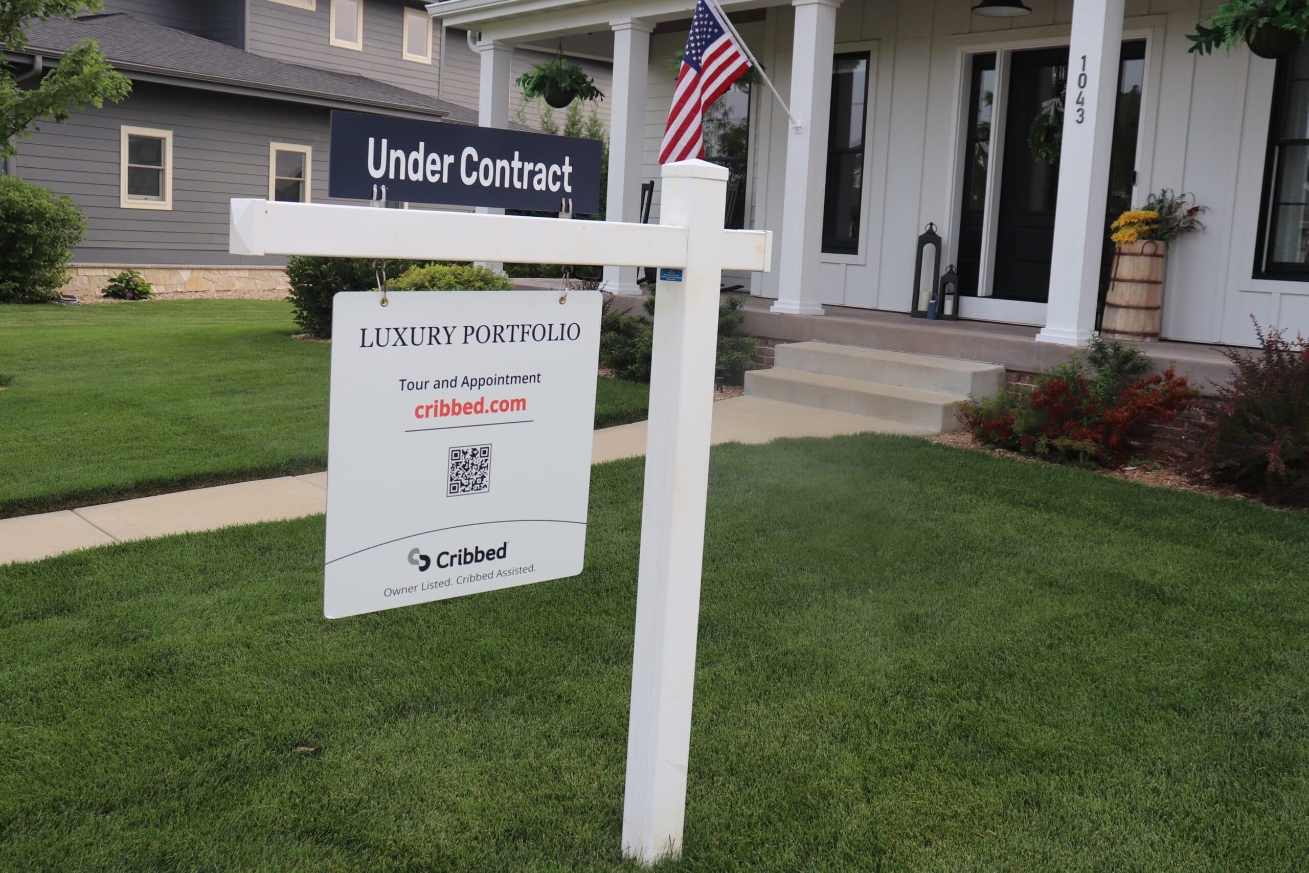 Cribbed yard sign with an Under Contract rider in front of a house