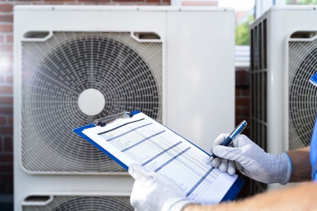 Home inspector filling in a checklist beside a home’s outdoor air conditioning unit