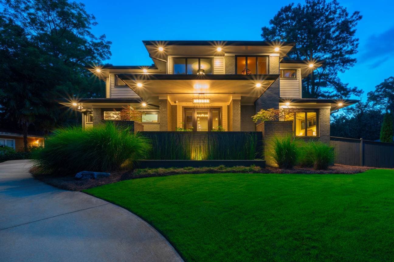 Modern two-story home lit up at dusk with a green front lawn