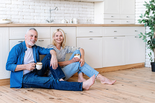 Smiling middle aged man and woman sitting on kitchen floor fun